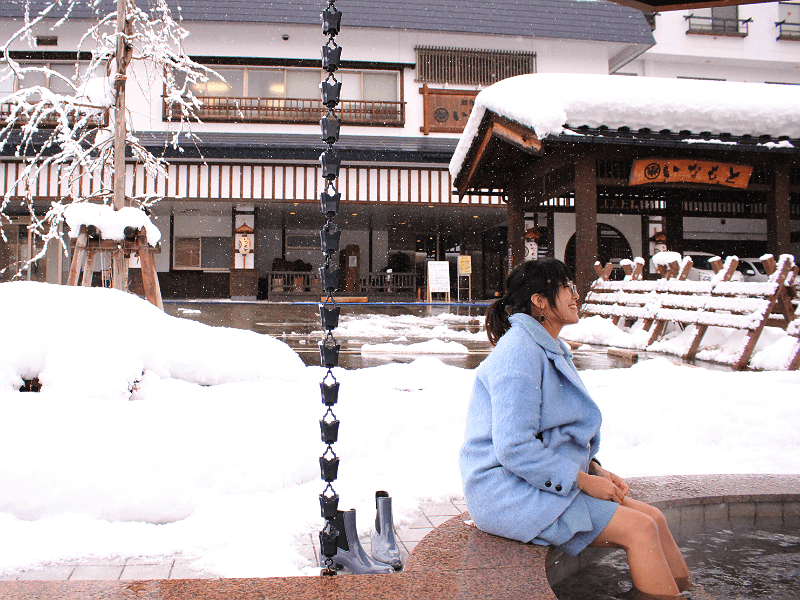 越後湯沢の冬景色のなか、女性が足湯に入っている写真