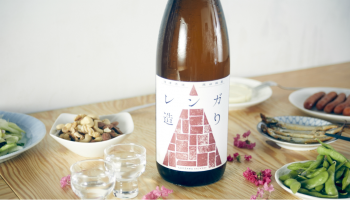 日本酒のオンラインストア「KURAND」と滝澤酒造株式会社(埼玉県深谷市)が共同開発した新ブランドの日本酒「レンガ造り」のボトル、まわりに枝豆などのおつまみがある写真