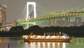 レインボウブリッジを背景に、夜の東京湾に浮かぶ屋形船の写真