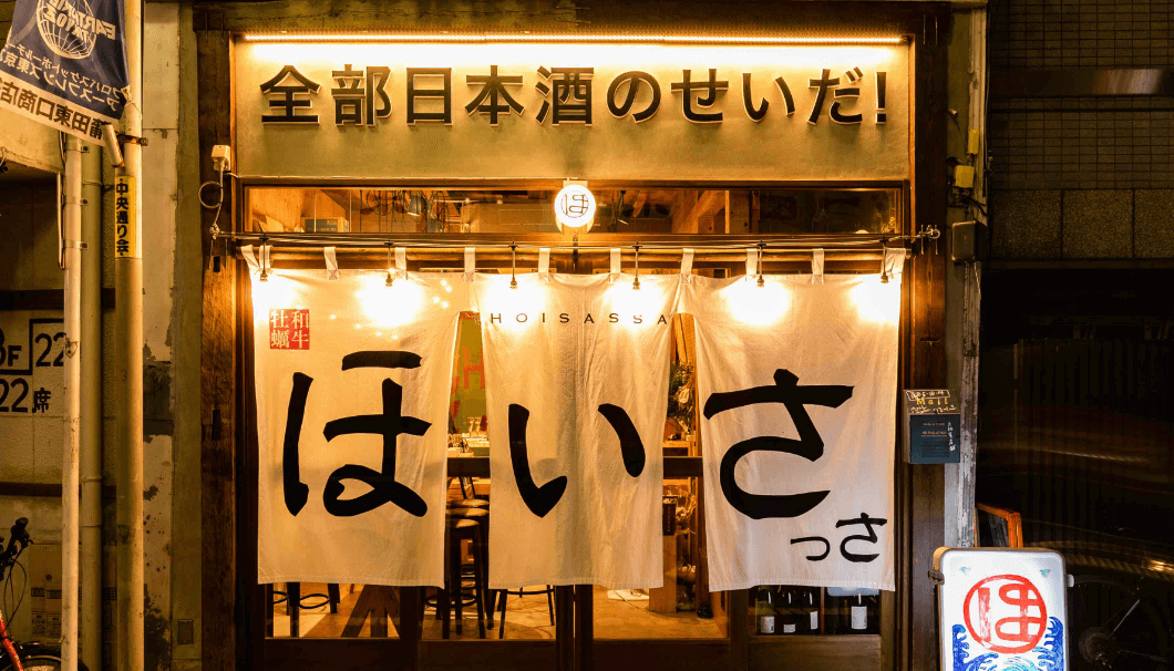 「全部日本酒のせいだ！」の看板と「牡蠣と和牛 ほいさっさ 蒲田店」の店構えの写真