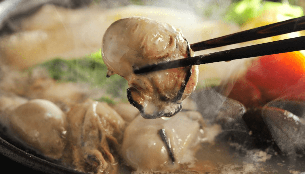 牡蠣鍋からお箸で牡蠣をつまみあげている写真