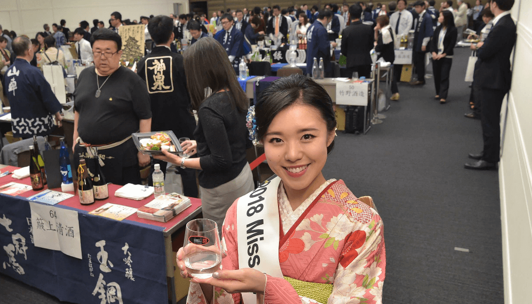 「ワイングラスでおいしい日本酒アワード」お披露目会会場で、お酒を持って微笑むミス日本酒の女性
