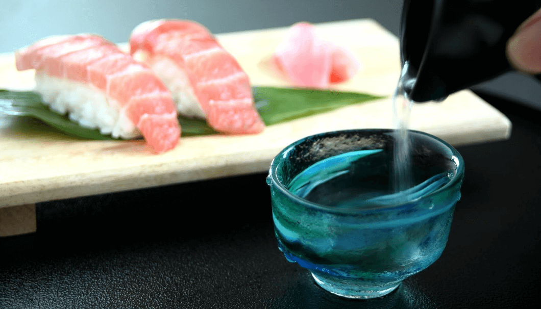 寿司の前にあるぐい呑に日本酒がそそがれている写真